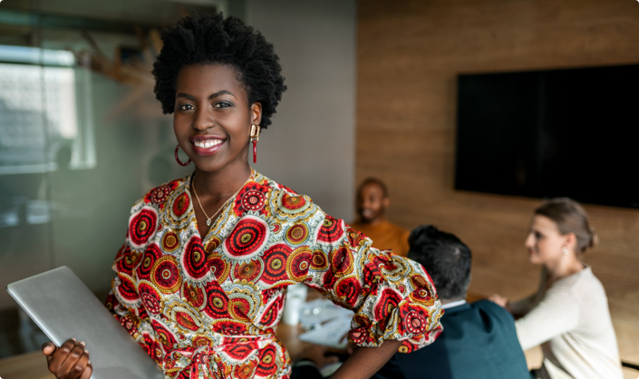 Woman holding laptop, smiling at the camera, people in background having a conversation